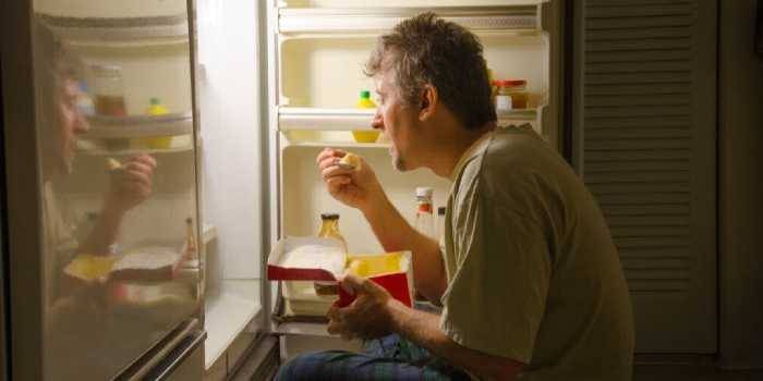 Мужчина ест мороженое у холодильника