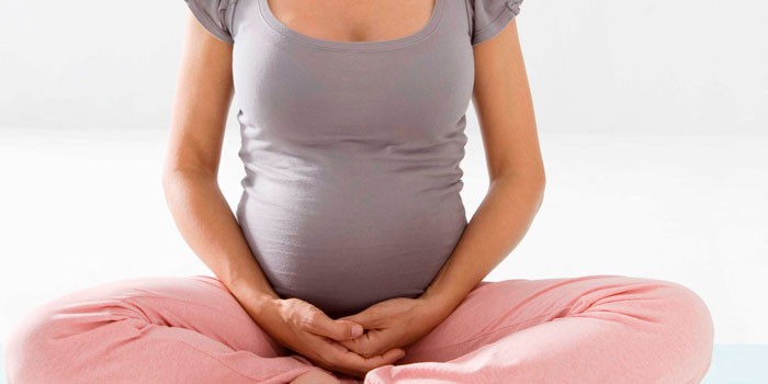 Беременная девушка сидит в позе лотоса